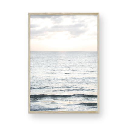 Fine art of vertical landscape print by Southern California photographer Kim Dybczak of Salt Creek Prints, featuring a bright image capturing pale blue ocean waves, light gray clouds in a bright sky. Gentle, small waves in the near and far distance. The sky is a uniform, pale white, creating a soft, overcast atmosphere. Photograph in framed minimalist mock up