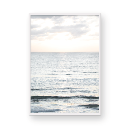 Fine art of vertical landscape print by Southern California photographer Kim Dybczak of Salt Creek Prints, featuring a bright image capturing pale blue ocean waves, light gray clouds in a bright sky. Gentle, small waves in the near and far distance. The sky is a uniform, pale white, creating a soft, overcast atmosphere. Photograph in framed minimalist mock up