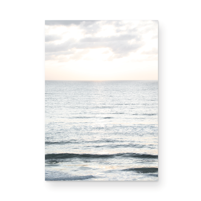 Fine art of vertical landscape print by Southern California photographer Kim Dybczak of Salt Creek Prints, featuring a bright image capturing pale blue ocean waves, light gray clouds in a bright sky. Gentle, small waves in the near and far distance. The sky is a uniform, pale white, creating a soft, overcast atmosphere. Photograph in unframed minimalist mock up