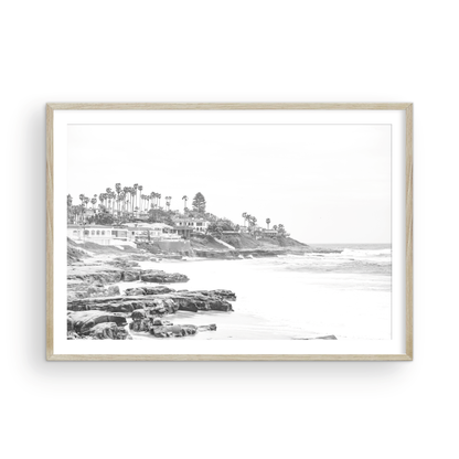 Fine art of WindanSea Beach, La Jolla California horizontal landscape black and white print by Southern California photographer Kim Dybczak of Salt Creek Prints, featuring a powerful waves crashing against the rocky shore of California coast. Beach homes and palm trees sit atop the cliffside, with stairs leading down to a sheltered area. Photograph in minimalist framed mock up