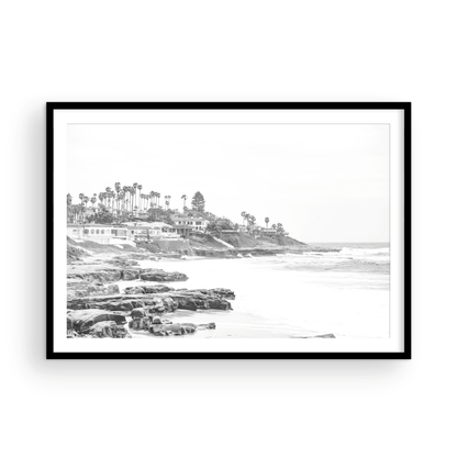 Fine art of WindanSea Beach, La Jolla California horizontal landscape black and white print by Southern California photographer Kim Dybczak of Salt Creek Prints, featuring a powerful waves crashing against the rocky shore of California coast. Beach homes and palm trees sit atop the cliffside, with stairs leading down to a sheltered area. Photograph in minimalist framed mock up