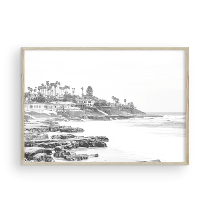 Fine art of WindanSea Beach, La Jolla California horizontal landscape black and white print by Southern California photographer Kim Dybczak of Salt Creek Prints, featuring a powerful waves crashing against the rocky shore of California coast. Beach homes and palm trees sit atop the cliffside, with stairs leading down to a sheltered area. Photograph in minimalist framed mock up