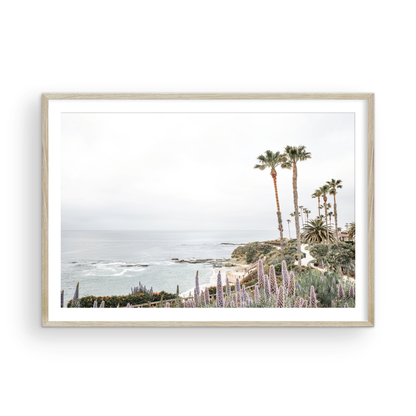 Horizontal coastal photography featuring a scenic view of the ocean with palm trees in the background, set against a white sky, located in Laguna California. Photograph in minimalist mock up.