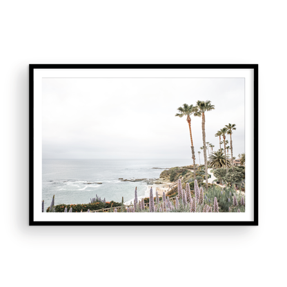 Horizontal coastal photography featuring a scenic view of the ocean with palm trees in the background, set against a white sky, located in Laguna California. Photograph in minimalist mock up.