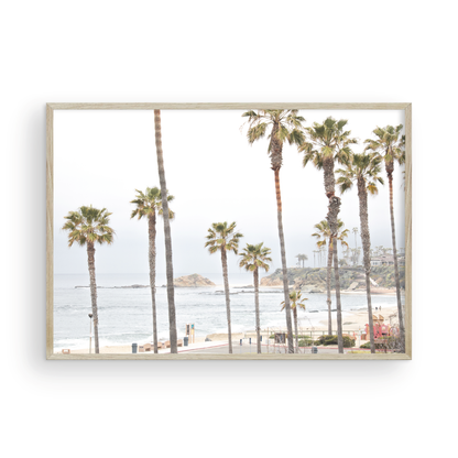 Horizontal coastal photography of a beachscape at Laguna Beach, California, beach art print featuring palm trees and a clear blue sky with a few clouds over a beach scene. Photograph in minimalist mock up.