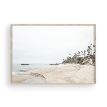 Horizontal coastal photography of a white lifeguard tower at Laguna Beach, California, depicting a beach scene with palm trees and a calm ocean. Photograph in minimalist mock up.