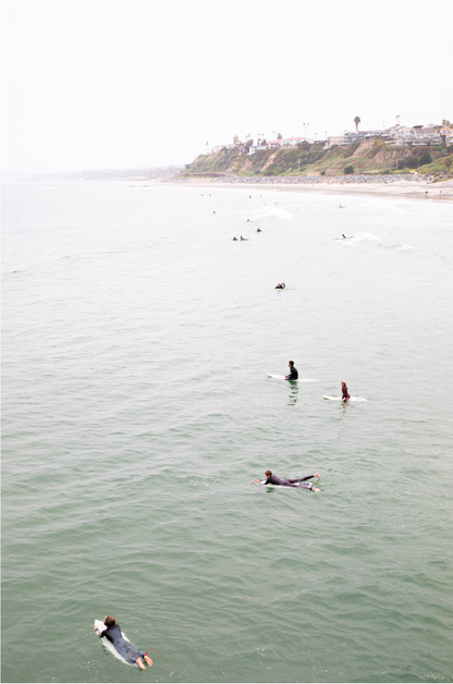 Vertical surf print of surfers floating in the ocean waves at a Southern California beach, with a distant coastline. This image captures surfing art and a minimalist surf vibe.