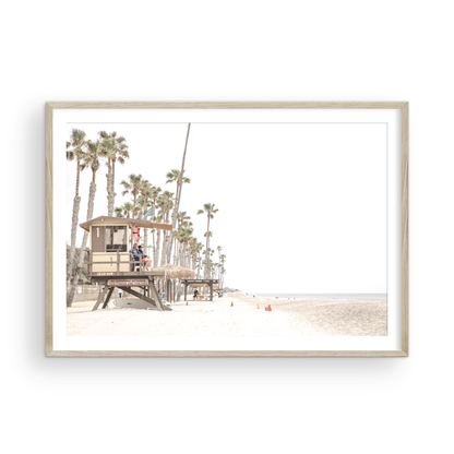 A wide landscape coastal photography view of San Clemente State Beach in Southern California, featuring a row of tall palm trees, a lifeguard tower, and people enjoying the calm beach. This image evokes Summer Vibes Wall Art and tropical beach print aesthetics. Photograph in minimalist mock up.