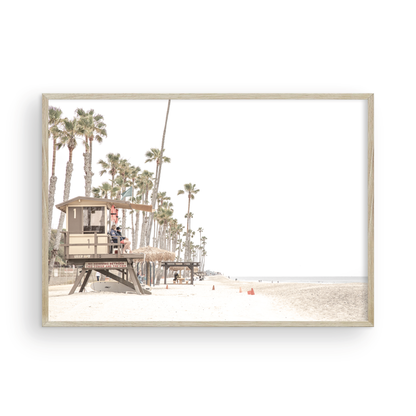A wide landscape coastal photography view of San Clemente State Beach in Southern California, featuring a row of tall palm trees, a lifeguard tower, and people enjoying the calm beach. This image evokes Summer Vibes Wall Art and tropical beach print aesthetics. Photograph in minimalist mock up.