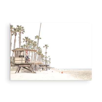 A wide landscape coastal photography view of San Clemente State Beach in Southern California, featuring a row of tall palm trees, a lifeguard tower, and people enjoying the calm beach. This image evokes Summer Vibes Wall Art and tropical beach print aesthetics. Photograph in minimalist mock up.
