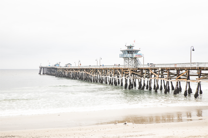 A long wooden pier, the San Clemente Pier, extends into the ocean in this landscape coastal photography. The beach in the foreground suggests a calm ocean print, ideal for a large coastal wall art or a beach cottage wall decor. 