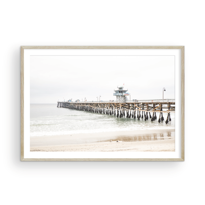 A long wooden pier, the San Clemente Pier, extends into the ocean in this landscape coastal photography. The beach in the foreground suggests a calm ocean print, ideal for a large coastal wall art or a beach cottage wall decor. Photograph in minimalist mock up.