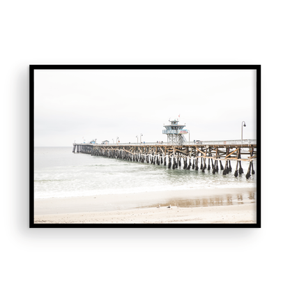 A long wooden pier, the San Clemente Pier, extends into the ocean in this landscape coastal photography. The beach in the foreground suggests a calm ocean print, ideal for a large coastal wall art or a beach cottage wall decor. Photograph in minimalist mock up.