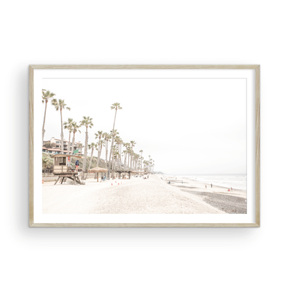 A wide landscape coastal photography view of San Clemente State Beach in Southern California, featuring a row of tall palm trees, a lifeguard tower, and people enjoying the calm beach. This horizontal image evokes Summer Vibes Wall Art and tropical beach print aesthetics. Photograph in minimalist mock up.