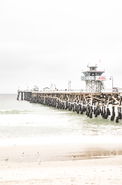A long wooden pier, the San Clemente Pier, extends into the ocean in this vertical coastal photography. The beach in the foreground suggests a calm ocean print, ideal for a large coastal wall art or a beach cottage wall decor. 