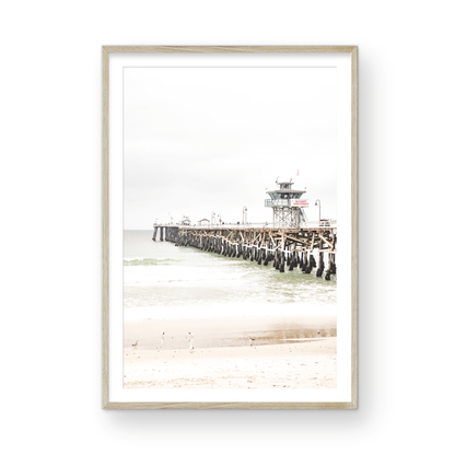 A long wooden pier, the San Clemente Pier, extends into the ocean in this vertical coastal photography. The beach in the foreground suggests a calm ocean print, ideal for a large coastal wall art or a beach cottage wall decor. Photograph in minimalist mock up.