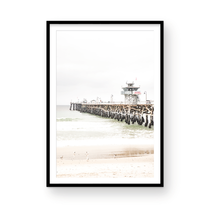 A long wooden pier, the San Clemente Pier, extends into the ocean in this vertical coastal photography. The beach in the foreground suggests a calm ocean print, ideal for a large coastal wall art or a beach cottage wall decor. Photograph in minimalist mock up.