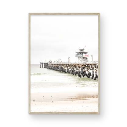 A long wooden pier, the San Clemente Pier, extends into the ocean in this vertical coastal photography. The beach in the foreground suggests a calm ocean print, ideal for a large coastal wall art or a beach cottage wall decor. Photograph in minimalist mock up.
