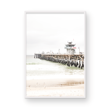 A long wooden pier, the San Clemente Pier, extends into the ocean in this vertical coastal photography. The beach in the foreground suggests a calm ocean print, ideal for a large coastal wall art or a beach cottage wall decor. Photograph in minimalist mock up.