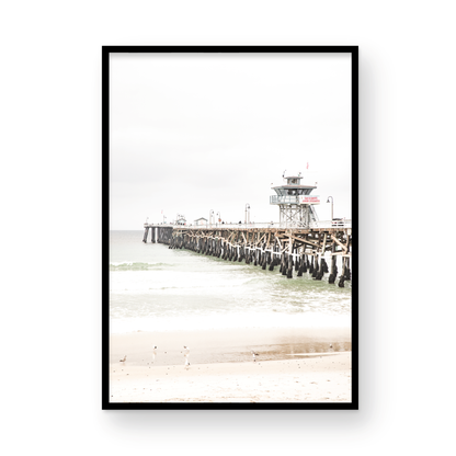 A long wooden pier, the San Clemente Pier, extends into the ocean in this vertical coastal photography. The beach in the foreground suggests a calm ocean print, ideal for a large coastal wall art or a beach cottage wall decor. Photograph in minimalist mock up.