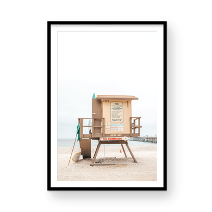 A vertical beach art close-up of a rustic lifeguard tower on San Clemente Beach, with a surfboard leaning against it and the pier visible in the distance. This image is perfect for a minimalist surf wall decor, surf nursery decor, or a fun surf print. Photograph in minimalist mock up.