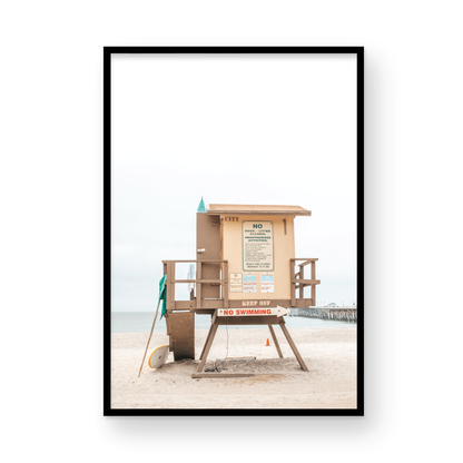 A vertical beach art close-up of a rustic lifeguard tower on San Clemente Beach, with a surfboard leaning against it and the pier visible in the distance. This image is perfect for a minimalist surf wall decor, surf nursery decor, or a fun surf print. Photograph in minimalist mock up.