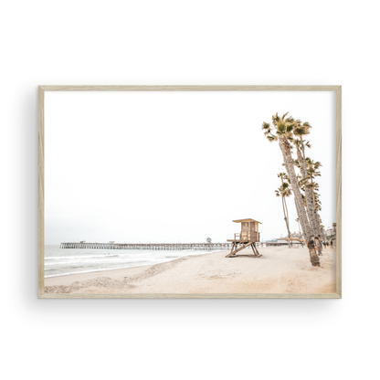 A wide landscape coastal photography view of San Clemente State Beach in Southern California, featuring a row of tall palm trees, a lifeguard tower, and people enjoying the calm beach. This image evokes Summer Vibes Wall Art and tropical beach print aesthetics. Photograph in minimalist mock up.