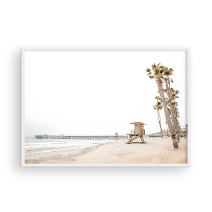 A wide landscape coastal photography view of San Clemente State Beach in Southern California, featuring a row of tall palm trees, a lifeguard tower, and people enjoying the calm beach. This image evokes Summer Vibes Wall Art and tropical beach print aesthetics. Photograph in minimalist mock up.