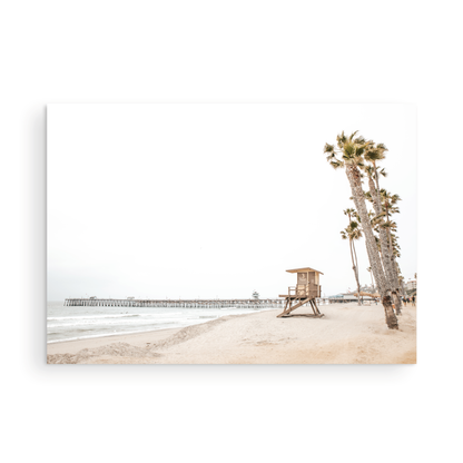 A wide landscape coastal photography view of San Clemente State Beach in Southern California, featuring a row of tall palm trees, a lifeguard tower, and people enjoying the calm beach. This image evokes Summer Vibes Wall Art and tropical beach print aesthetics. Photograph in minimalist mock up.