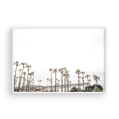 Horizontal landscape coastal photography of many palm trees in the foreground, with the San Clemente Pier extending into the ocean in the background. This large landscape beach art conveys strong beach vibes. Photograph in minimalist mock up.