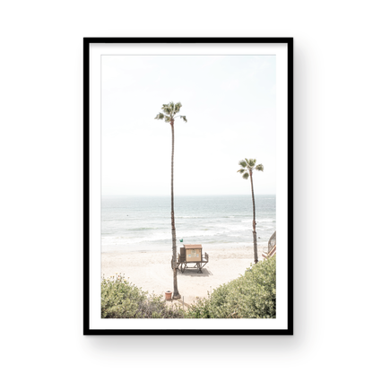 Vertical beach wall art featuring a lifeguard tower nestled between two tall palm trees on a sunny California beach, capturing a serene beach vibe. Photograph in minimalist mock up.