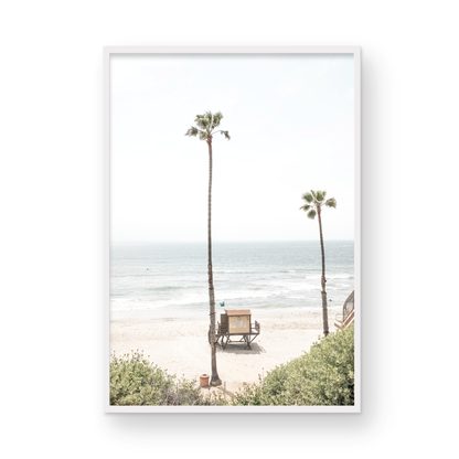 Vertical beach wall art featuring a lifeguard tower nestled between two tall palm trees on a sunny California beach, capturing a serene beach vibe. Photograph in minimalist mock up.