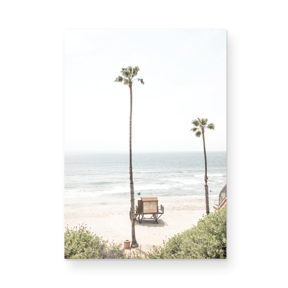 Vertical beach wall art featuring a lifeguard tower nestled between two tall palm trees on a sunny California beach, capturing a serene beach vibe. Photograph in minimalist mock up.