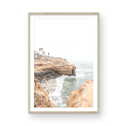 Fine art of Sunset Cliffs, San Diego California vertical print of hazy high-angle landscape beach photography captures a light blue ocean meeting tall tan, rocky, brown cliffs rise as iconic coastal scenery. Photograph in minimalist mock up.