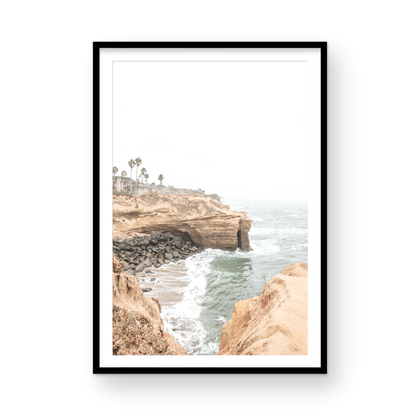 Fine art of Sunset Cliffs, San Diego California vertical print of hazy high-angle landscape beach photography captures a light blue ocean meeting tall tan, rocky, brown cliffs rise as iconic coastal scenery. Photograph in minimalist mock up.