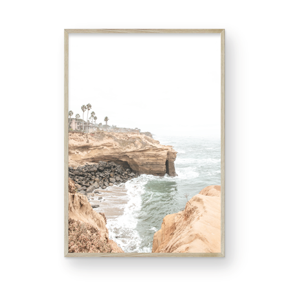 Fine art of Sunset Cliffs, San Diego California vertical print of hazy high-angle landscape beach photography captures a light blue ocean meeting tall tan, rocky, brown cliffs rise as iconic coastal scenery. Photograph in minimalist mock up.