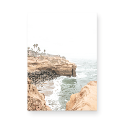 Fine art of Sunset Cliffs, San Diego California vertical print of hazy high-angle landscape beach photography captures a light blue ocean meeting tall tan, rocky, brown cliffs rise as iconic coastal scenery. Photograph in minimalist mock up.