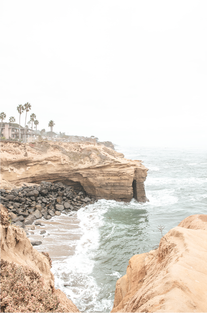 Fine art of Sunset Cliffs, San Diego California vertical print of hazy high-angle landscape beach photography captures a light blue ocean meeting tall tan, rocky, brown cliffs rise as iconic coastal scenery.