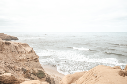 Fine art of Sunset Cliffs, San Diego California horizontal print of hazy high-angle landscape beach photography captures a light blue ocean meeting tall tan and brown cliffs rise as iconic coastal scenery. 