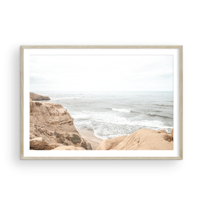 Fine art of Sunset Cliffs, San Diego California horizontal print of hazy high-angle landscape beach photography captures a light blue ocean meeting tall tan and brown cliffs rise as iconic coastal scenery. Photograph in minimalist mock up.