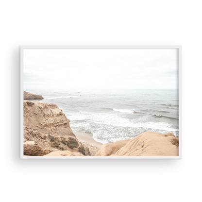 Fine art of Sunset Cliffs, San Diego California horizontal print of hazy high-angle landscape beach photography captures a light blue ocean meeting tall tan and brown cliffs rise as iconic coastal scenery. Photograph in minimalist mock up.