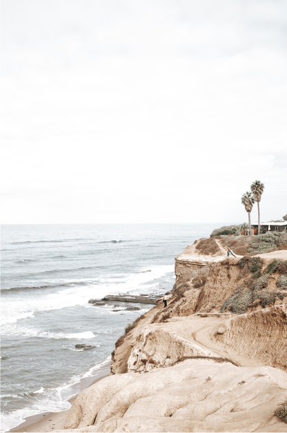 Fine art of Sunset Cliffs, San Diego California vertical print of hazy high-angle landscape beach photography captures a light blue ocean meeting tall tan and brown cliffs rise as iconic coastal scenery. 