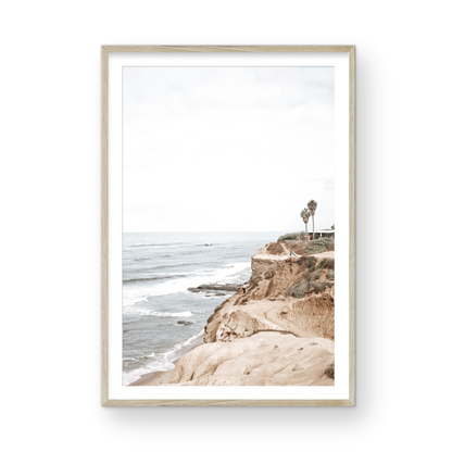 Fine art of Sunset Cliffs, San Diego California vertical print of hazy high-angle landscape beach photography captures a light blue ocean meeting tall tan and brown cliffs rise as iconic coastal scenery. Photograph in minimalist mock up.