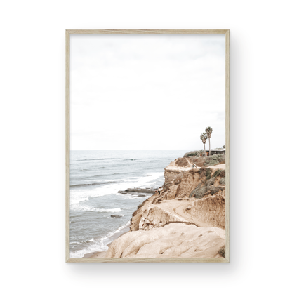 Fine art of Sunset Cliffs, San Diego California vertical print of hazy high-angle landscape beach photography captures a light blue ocean meeting tall tan and brown cliffs rise as iconic coastal scenery. Photograph in minimalist mock up.