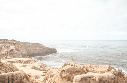 Fine art of Sunset Cliffs, San Diego California horizontal print of hazy high-angle landscape beach photography captures a light blue ocean meeting tall tan and brown cliffs rise as iconic coastal scenery. 