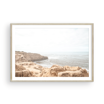 Fine art of Sunset Cliffs, San Diego California horizontal print of hazy high-angle landscape beach photography captures a light blue ocean meeting tall tan and brown cliffs rise as iconic coastal scenery. Photograph in minimalist art mock up.
