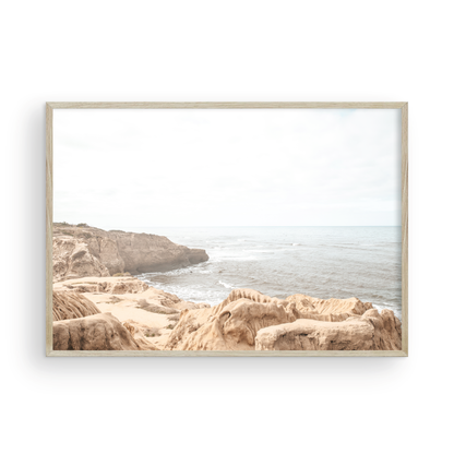 Fine art of Sunset Cliffs, San Diego California horizontal print of hazy high-angle landscape beach photography captures a light blue ocean meeting tall tan and brown cliffs rise as iconic coastal scenery. Photograph in minimalist mock up.