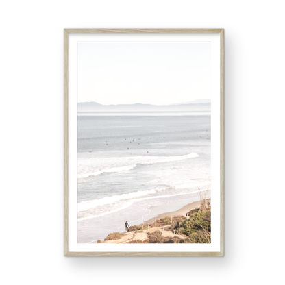 Minimalist ocean print of ocean waves with surfers in the distance and a sandy hillside in the foreground. 