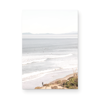 Minimalist ocean print of ocean waves with surfers in the distance and a sandy hillside in the foreground. 