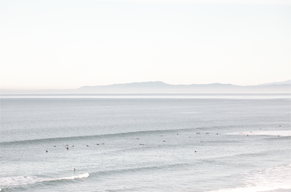 Coastal photography featuring a calm ocean scene with gentle waves and a hazy horizon line, predominantly in blue and white tones. 